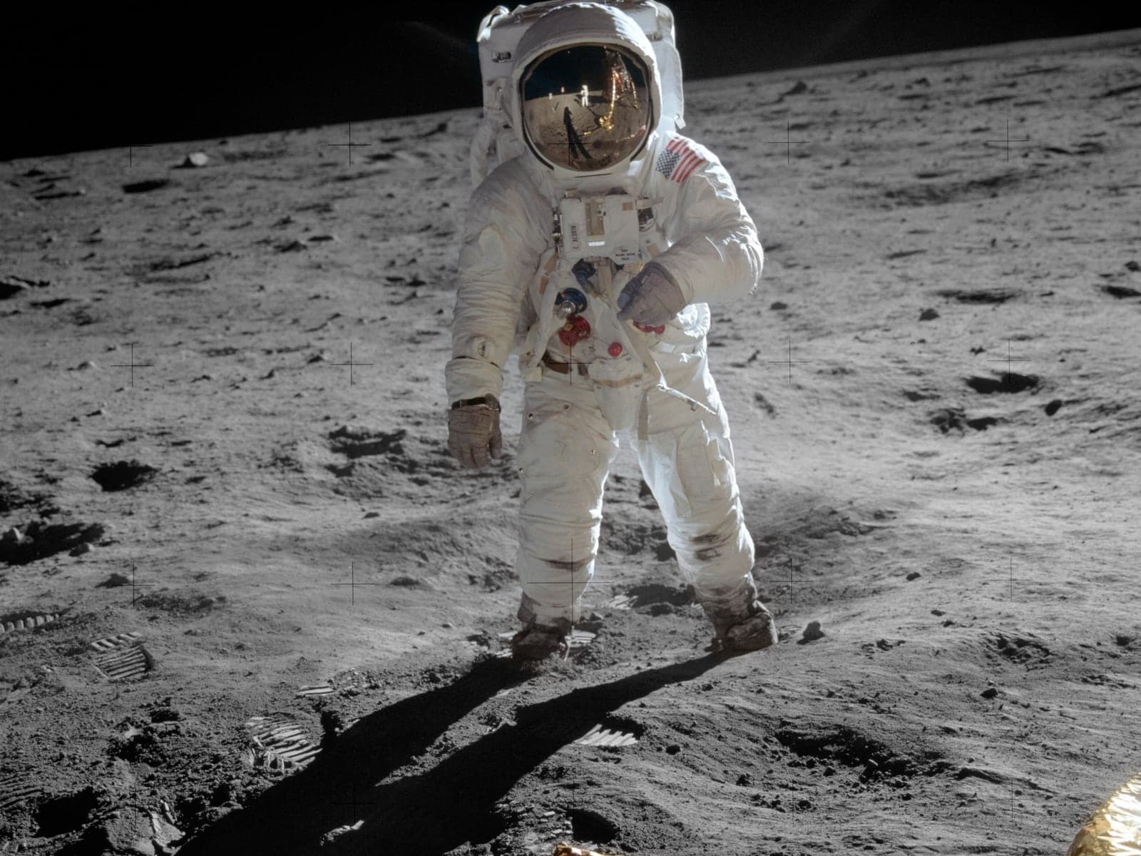 Buzz Aldrin standing on the lunar surface in a white spacesuit, Neil Armstrong reflected in his visor.
