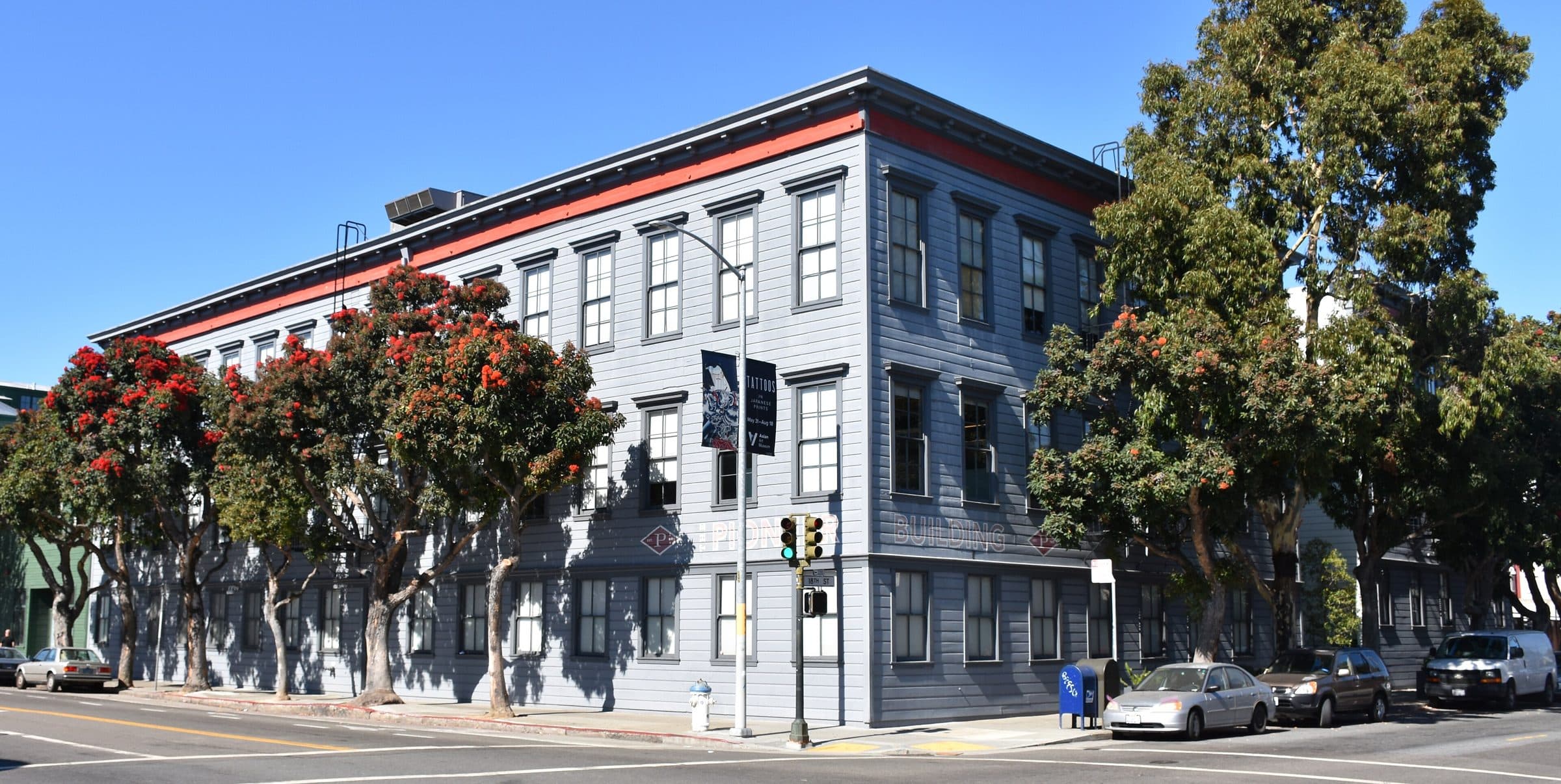 The Pioneer Building in San Francisco, a gray three-story corner building with a red cornice and flowering trees along the street.
